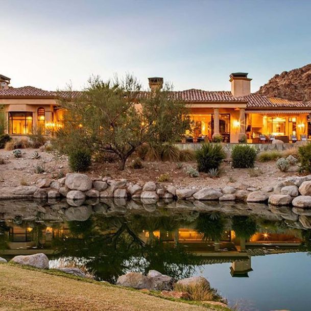 Sunset view of home in front of pond with lights on